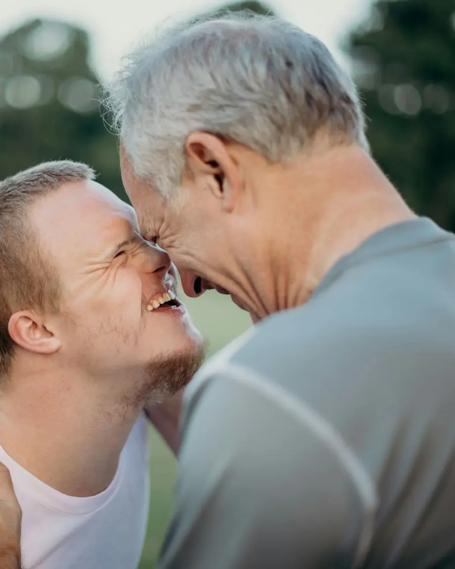 A young man and his father touching foreheads and laughing outdoors