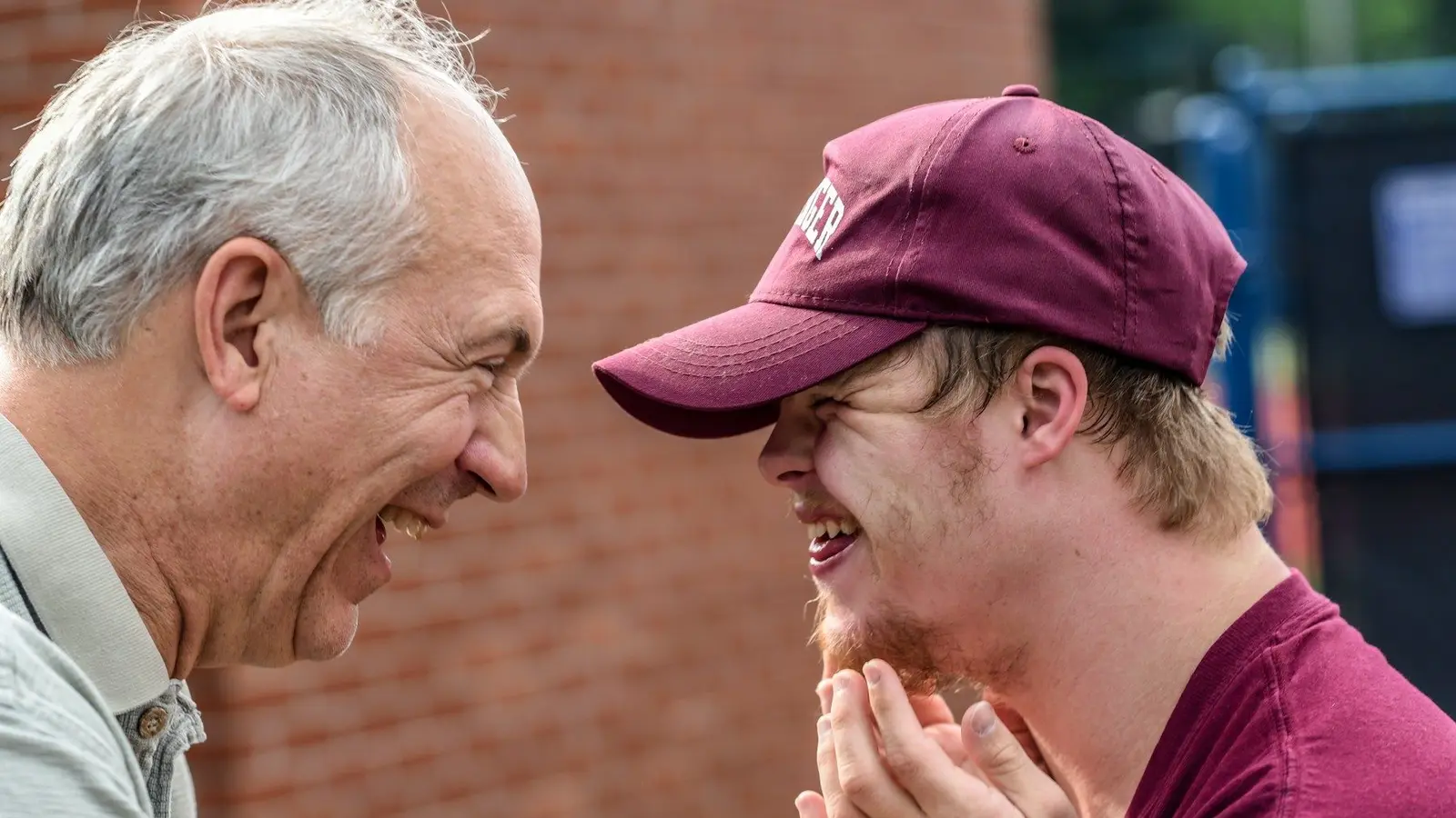 An older man and a young man in a cap laughing together outdoors