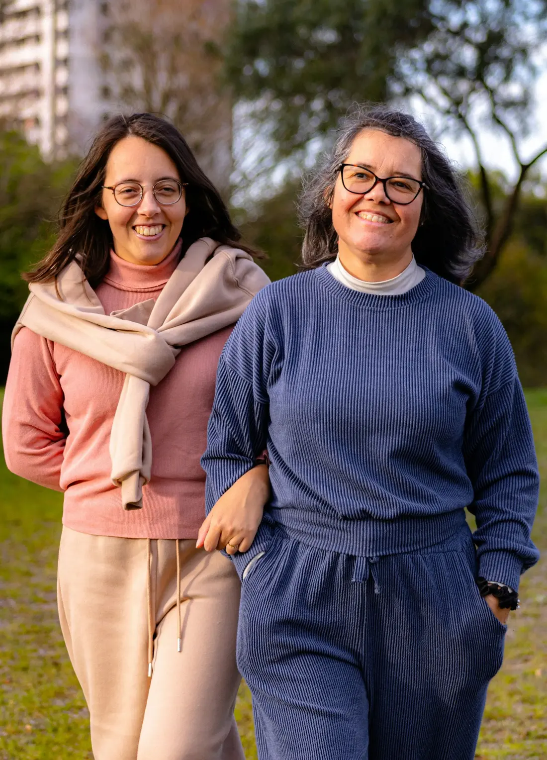 Two women walking arm in arm through a park, both smiling