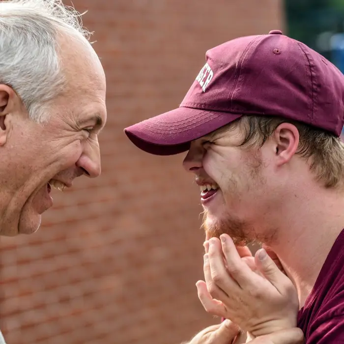 An older man and a young man in a cap laughing together outdoors