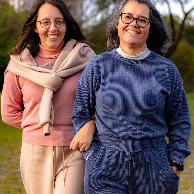 Two women walking arm in arm through a park, both smiling